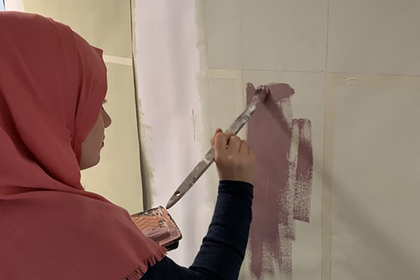 Eine junge Frau malt ein Feld auf einer Wand mit einem Pinsel aus.